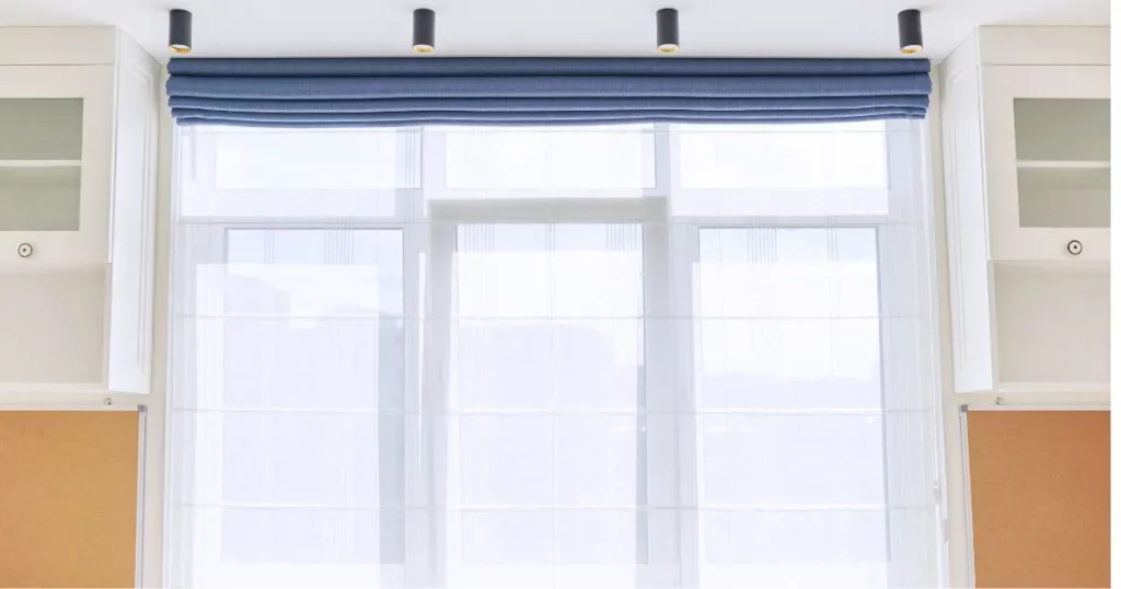 A white window with sheer Roman Shades and a blue valance, flanked by white cabinets in South Walton & 30A