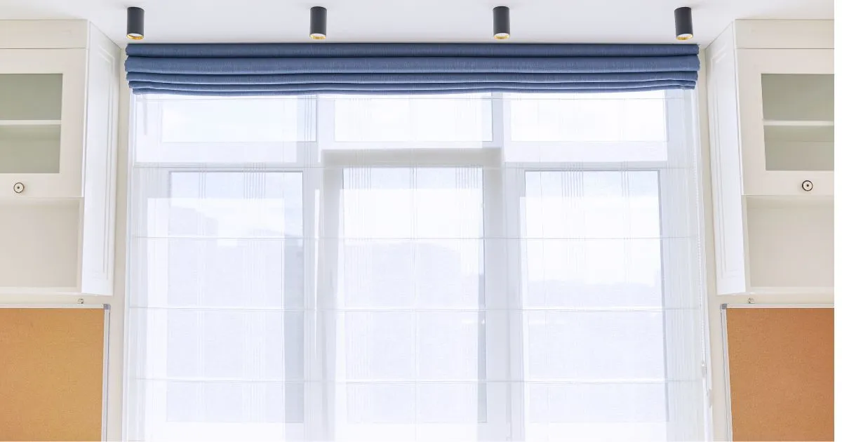 A white window with sheer Roman Shades and a blue valance, flanked by white cabinets in South Walton & 30A