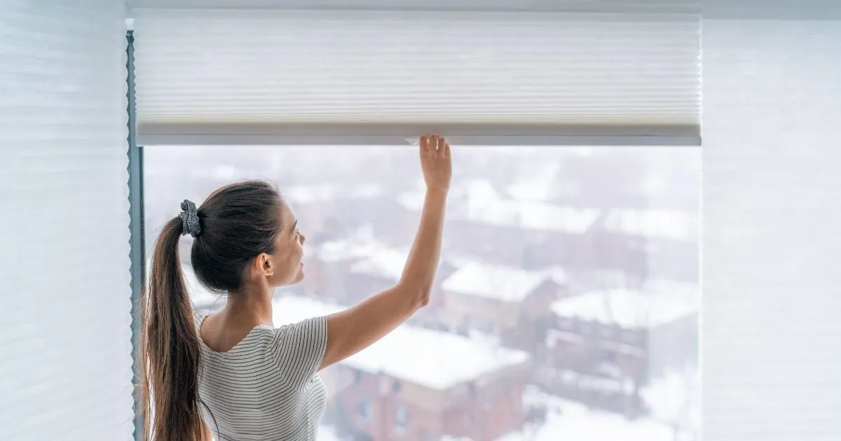 Woman opens white Honeycomb Shades overlooking snowy South Walton neighborhood